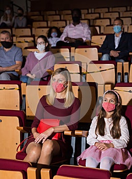 Woman with tween daughter in protective masks watching play in theater