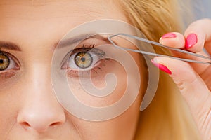 Woman tweezing eyebrows depilating with tweezers