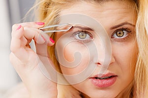 Woman tweezing eyebrows depilating with tweezers