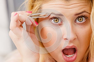 Woman tweezing eyebrows depilating with tweezers