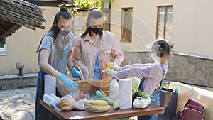 A woman with two daughters put food in a basket to help poor people. Delivery of food packages during the coronavirus