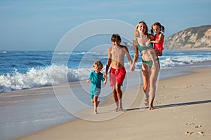 Woman and two kids, dressed for swim, have fun run on sand beach