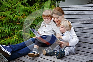 woman and two little siblings sitting on bench in park and reading book