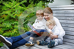 woman and two little siblings sitting on bench in park and reading book