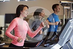 Woman and two young adults running on treadmills at a gym