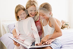 Woman and two young girls in bedroom reading book