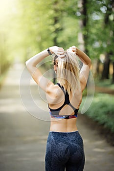 Woman tying hair in ponytail getting ready for exercising at sunset. Beautiful young sporty woman attaching her long hair in park.