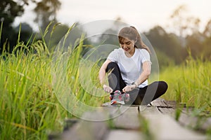 Woman tying her running shoes on wooden path in field