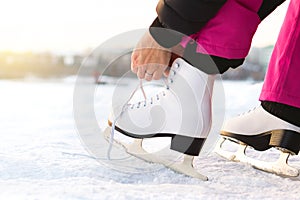 Woman tying ice skates laces by a lake or pond. Lacing iceskates. Skater about to exercise on an outdoor track or rink. Sunny win