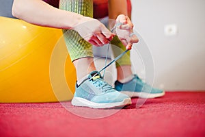 Woman tying shoe at gym, sitting on a fitness ball