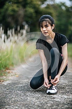 Woman tying shoelaces on concrete road to exercise in fresh atmosphere.