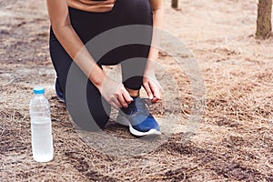 Woman tying up shoelaces when jogging in forest back with drinking water bottle beside hers. Sneakers rope tying. People and life