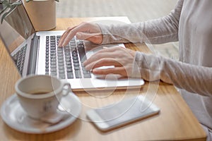 Woman typing on laptop computer and using smart phone