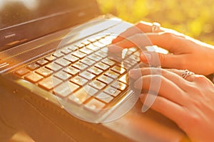Woman typing on a laptop keyboard in a warm sunny day outdoors.