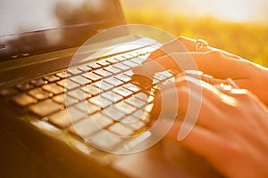 Woman typing on a laptop keyboard in a warm sunny day outdoors.