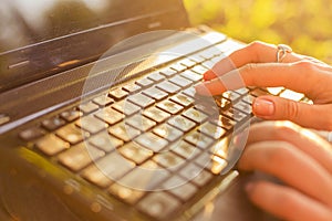 Woman typing on a laptop keyboard in a warm sunny day outdoors.