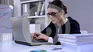 Woman typing on laptop, pile of documents lying on table, overload of work