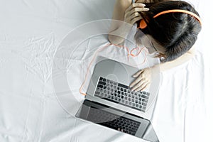 Woman typing laptop on white bed in morning. Young Asian girl us