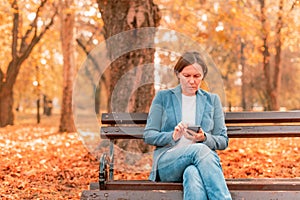 Woman typing text message on mobile phone on park bench