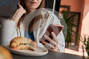 Woman typing text message on smart phone in a cafe. Cropped image of young woman sitting at a table with a coffee using