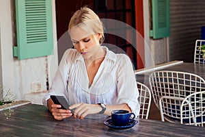 Woman typing text message on smart phone in a cafe. young woman sitting at a table with a coffee using mobile phone.