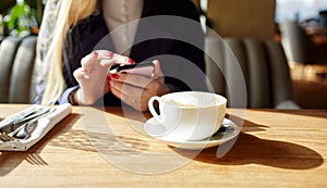Woman typing text message on smart phone in a cafe. Young woman sitting at a table with a coffee using mobile phone.