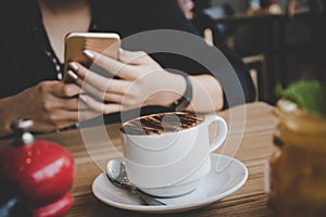 Woman typing text message on smart phone in a coffee shop. Cropped image of young woman sitting at a table with a coffee using