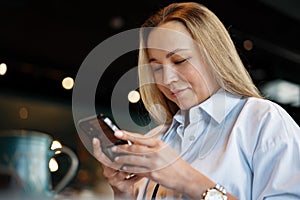 Woman typing text message on smart phone while sitting in a cafe