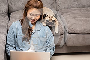 Woman typing and working on laptop with dog Pug breed lying on her knee