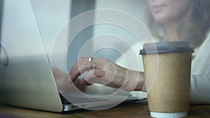 Woman typing and working with laptop while sitting at table in home office.