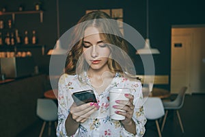 Woman typing write a message on a smartphone in a modern cafe. image of a young beautiful girl with coffee or cappuccino