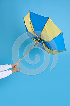 Woman with umbrella caught in gust of wind on light blue background, closeup