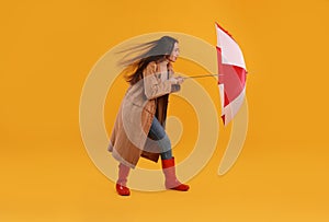 Woman with umbrella caught in gust of wind on yellow background