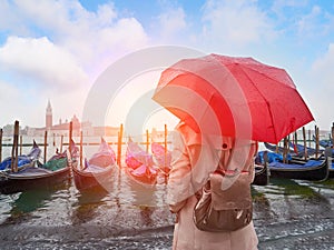 Woman with umbrella standing back and looking on gondolas. Venice. Italy