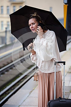 Woman with umbrella at train station holding phone