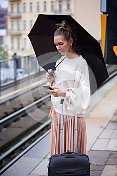 Woman with umbrella at train station looking at phone