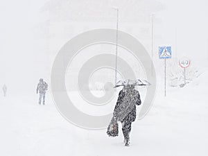 A woman with an umbrella walks along a snow-covered road following other people during a heavy snowfall