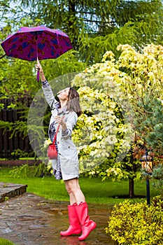 Woman with an umbrella, wearing red rubber boots and a raincoat in the rain in a blooming spring garden