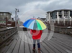 Woman under rainbow umbrella. Person walking with colorful umbrella on the pier at rainy day