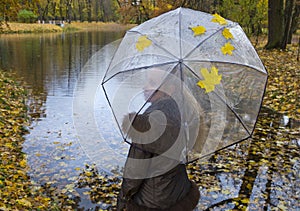 Woman under a transparent umbrella on autumn day on the river shore