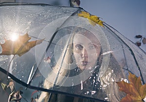 Woman under a transparent umbrella with autumn leaves