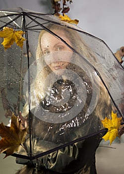 Woman under a transparent umbrella with autumn leaves.