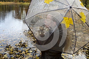 Woman under a transparent umbrella on a cloudy autumn day on the lake shore