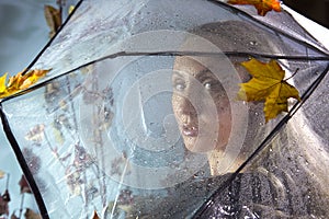 Woman under a transparent umbrella with raindrops with autumn leaves. Soft focus