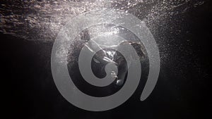 Woman under water surface in lights and bubbles of air, subaquatic shot, slow motion