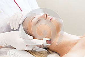 Woman undergoes the procedure of medical micro needle therapy with a modern medical instrument derma roller.