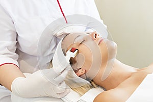 Woman undergoes the procedure of medical micro needle therapy with a modern medical instrument derma roller.