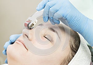 Woman undergoes the procedure of medical micro needle therapy with a modern medical instrument derma roller.