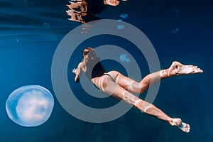 Woman underwater with big jellyfish in blue ocean. Free diver underwater in clear sea