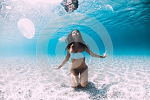 Woman underwater over sandy sea with jellyfish. Freediving in blue ocean